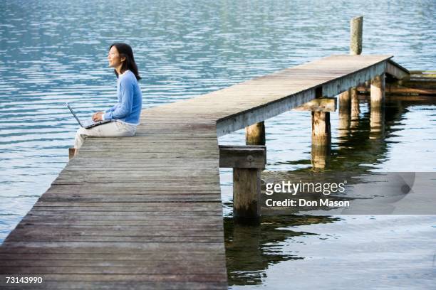 woman using laptop on edge of pier - profile laptop sitting stock-fotos und bilder