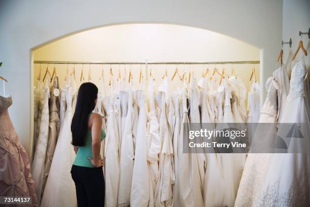 woman looking at wedding dresses on rack - trouwjurk stockfoto's en -beelden