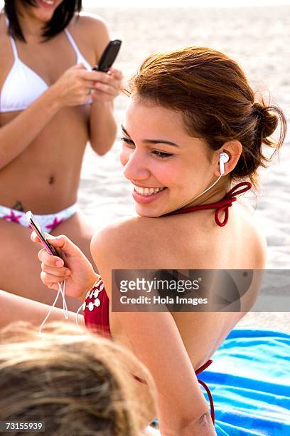 young women listening to music and talking on cell phone while sunbathing on beach - american sunbathing association photos et images de collection