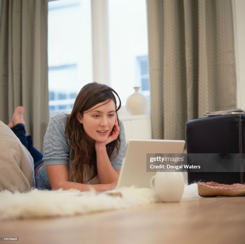 Young woman lying on floor, using laptop