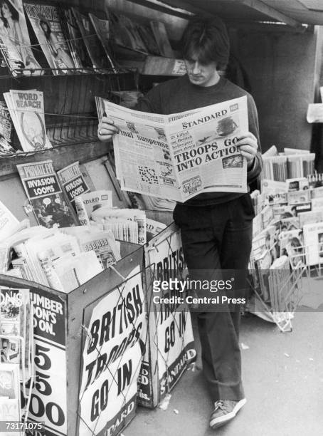 Man reads a copy of the Evening Standard at a London newsstand during the Falklands War, 1982. The headlines read 'Troops Go Into Action' and...