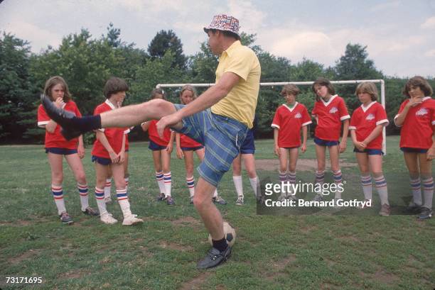 Girl's soccer team watches as their coach, dressed in a yellow shorts and checkered shorts, demonstrates kicking technique, Hicksville, Long Island,...