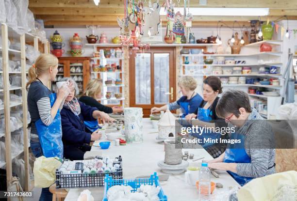 a group of people seated at a workbench in a pottery workshop, handbuilding clay objects. a woman with a cup of tea. - avondschool stockfoto's en -beelden