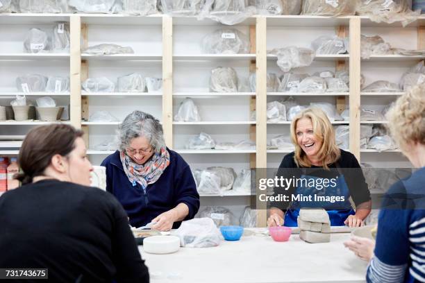 a group of four women chatting together and working on their pots in a pottery studio. - avondschool stockfoto's en -beelden