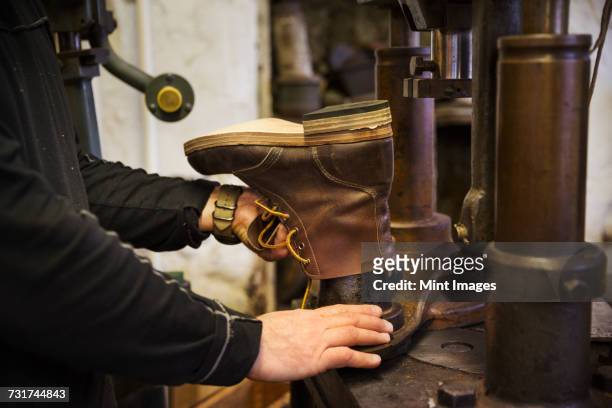 close up of worker in a shoemakers workshop, using a machine to make a leather ankle boot. - ankle boot stockfoto's en -beelden