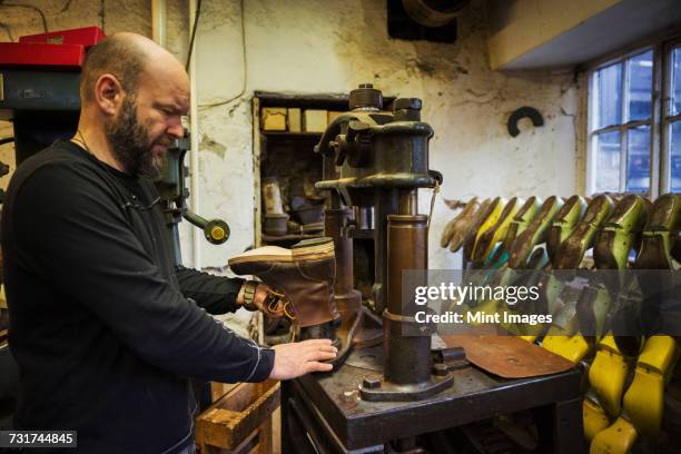 man standing in a shoemakers workshop, using a machine to make a leather ankle boot. - ankle boot stockfoto's en -beelden