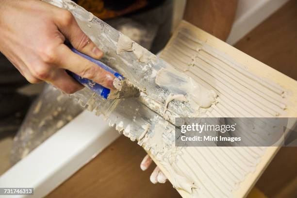 close up of a builder, tiler sitting in a bathtub spreading adhesive on a tile. - mörtel stock-fotos und bilder