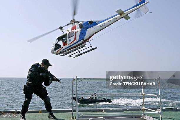 Member of the Malaysian Marine Police amphibious assault unit points his rifle down a stairway aboard the Japanese Coast Guard ship Yashima, while a...