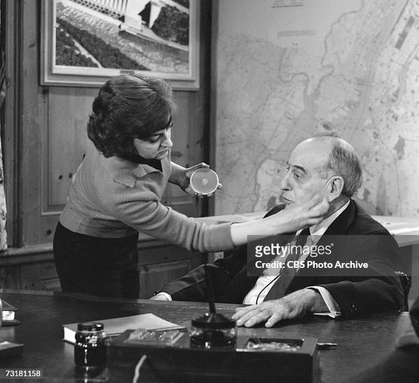American public official and city planner Robert Moses sits as his desk as a woman touches up his make-up prior to an interview for the CBS Reports...