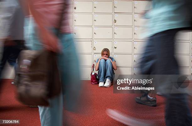 teenage girl (13-15) sitting by lockers in school hallway - vulnerability stock pictures, royalty-free photos & images