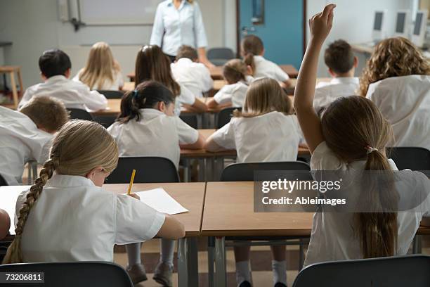 girl (8-10) raising hand in classroom, rear view - schulkinder stock-fotos und bilder