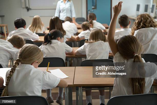girl (8-10) raising hand in classroom, rear view - teachers education uniform stockfoto's en -beelden