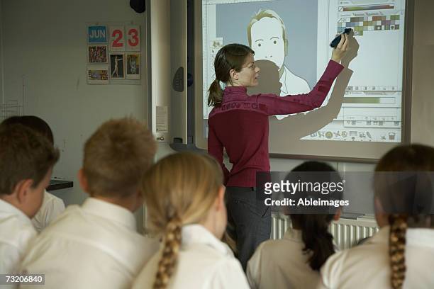 teacher pointing to video screen to students (8-10) in classroom, rear view - projector classroom photos et images de collection