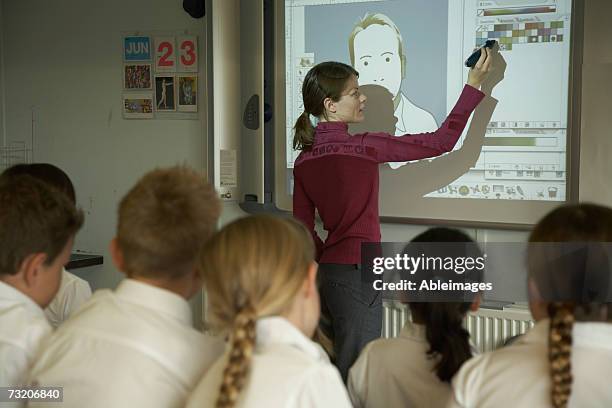 teacher pointing to video screen to students (8-10) in classroom, rear view - projection equipment stock pictures, royalty-free photos & images