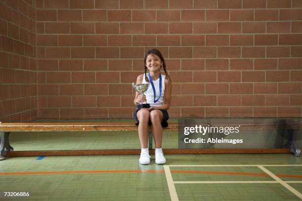 girl (10-12) sitting on bench in gym, with trophy - mädchen 10 12 stock-fotos und bilder