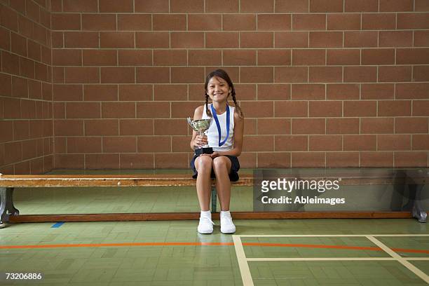 girl (10-12) sitting on bench in gym, with trophy - 13 year old girls in shorts stock pictures, royalty-free photos & images