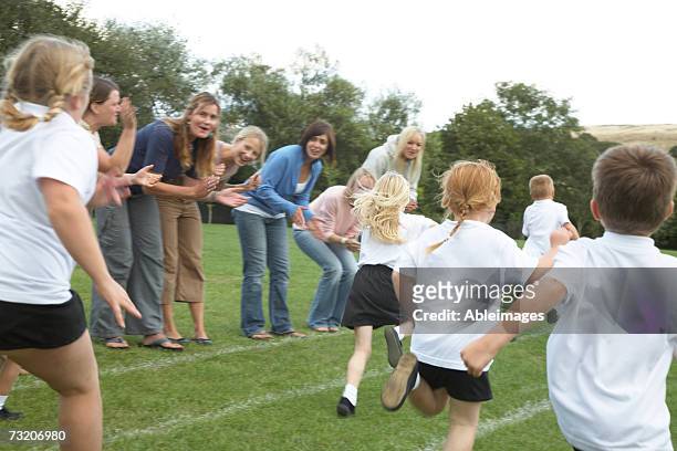 children (5-8) running on field, mothers cheering on sidelines - incidental people stock pictures, royalty-free photos & images