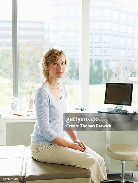 female patient sitting on exam table in exam room - examination table stock-fotos und bilder