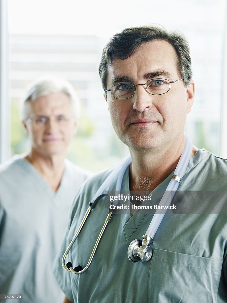 Male doctor posing in exam room colleague in background