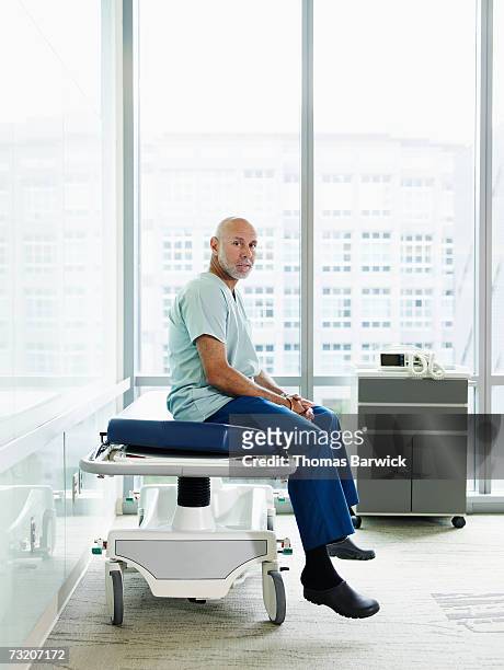 male surgeon sitting on gurney in hospital corridor - hospital gurney stock pictures, royalty-free photos & images