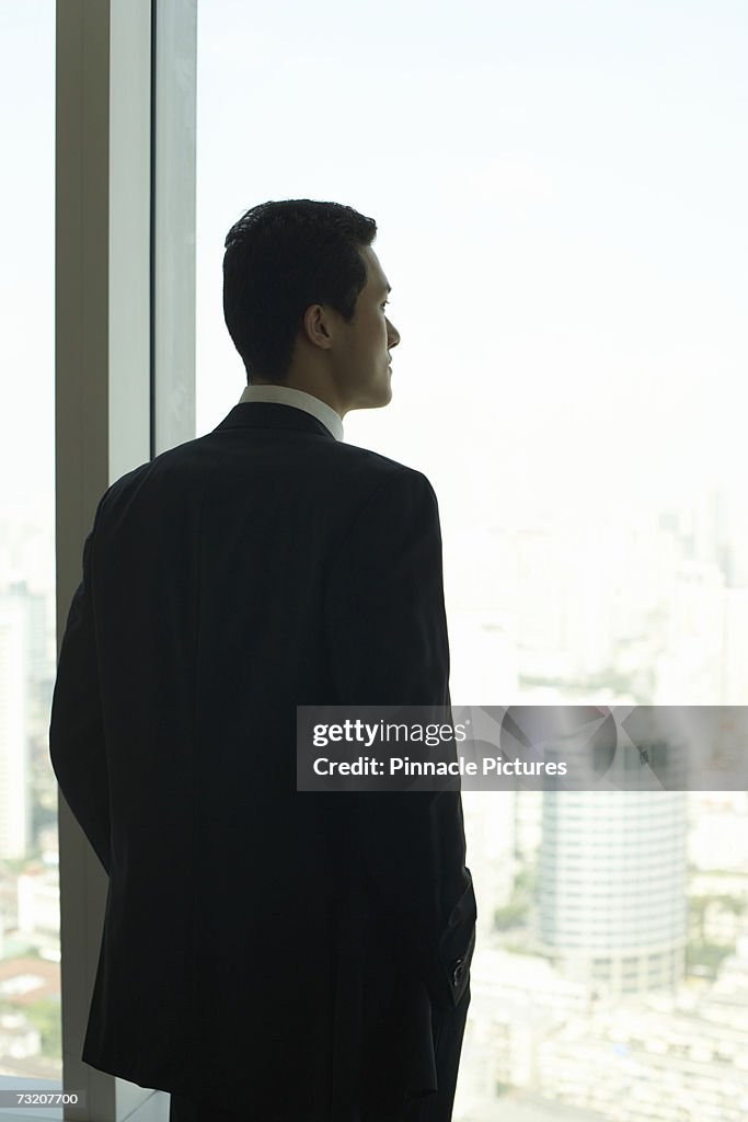 Businessman looking out of office window, rear view