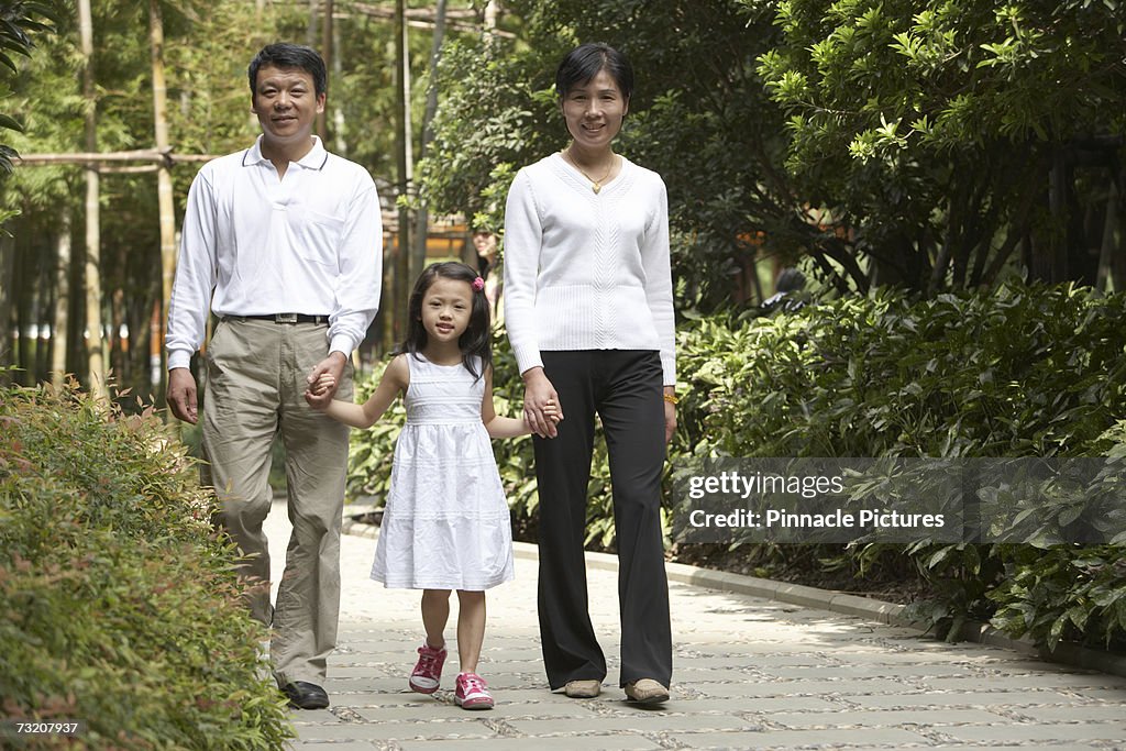 Parents walking with daughter (4-5) in park, portrait