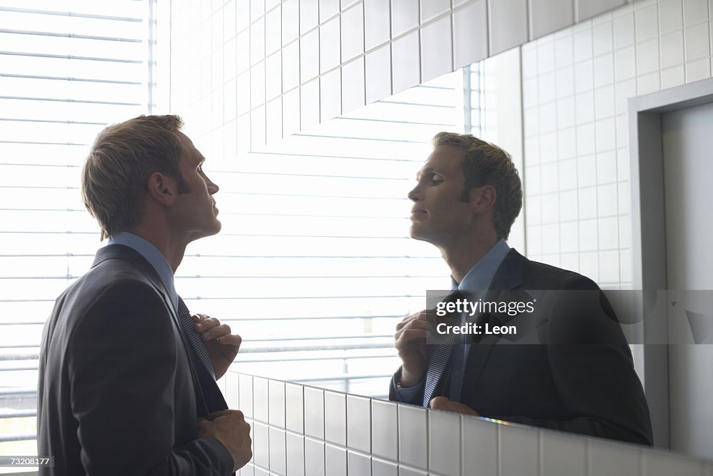 Businessman adjusting tie in bathroom mirror