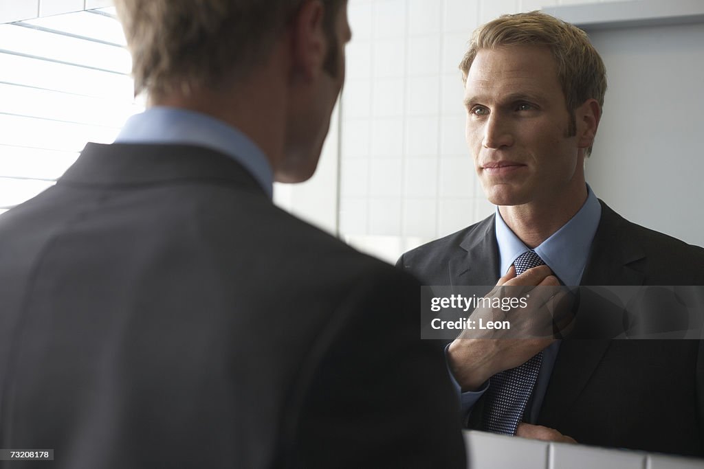 Businessman adjusting tie in bathroom mirror