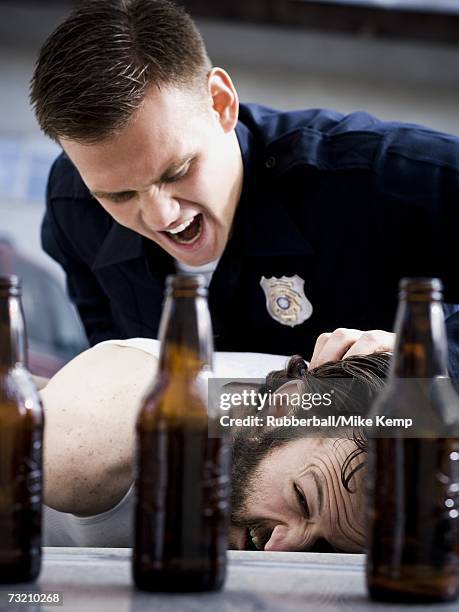 police officer arresting man lying down with beer bottles - police brutality stockfoto's en -beelden