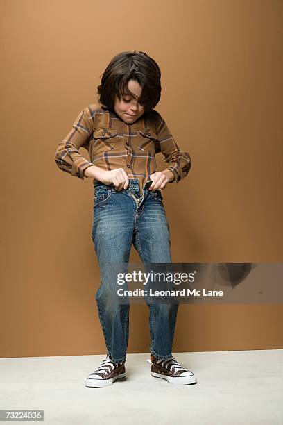 boy (8-9) struggling to fasten jeans button - stretto foto e immagini stock