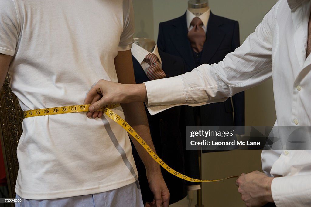 Fashion designer measuring man's waist with tape measure, mid section