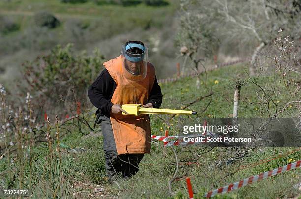 De-miner from Bac Tec International, on contract by the United Nations, probes with a yellow metal detector as he clears cluster bomblets, dropped by...