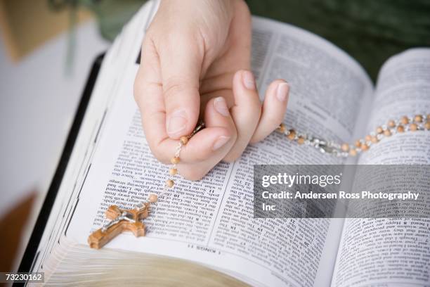 close up of woman holding rosary on open bible - gebetskette stock-fotos und bilder