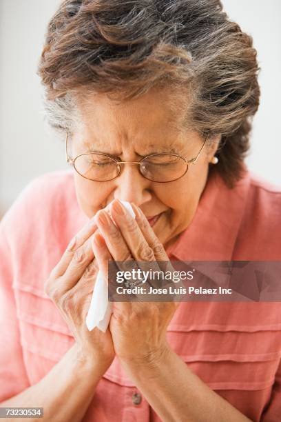 senior hispanic woman sneezing with tissue - closeup of a hispanic woman sneezing stock pictures, royalty-free photos & images