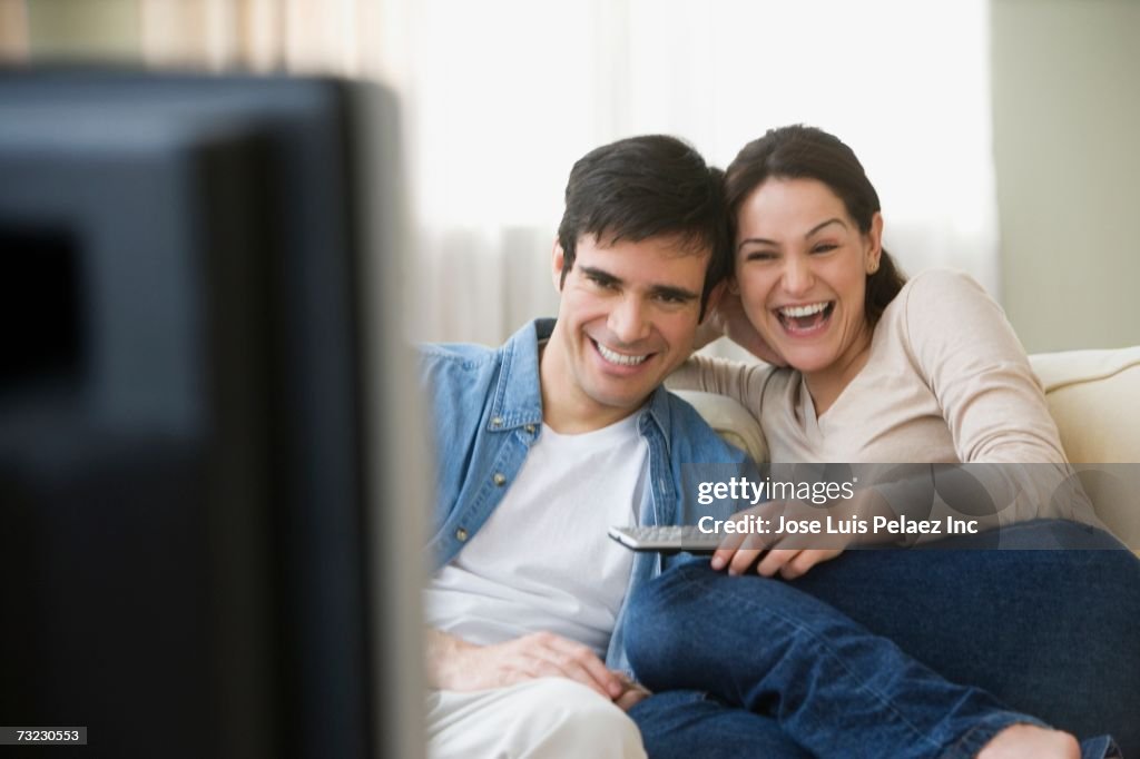 Couple watching television and laughing on sofa