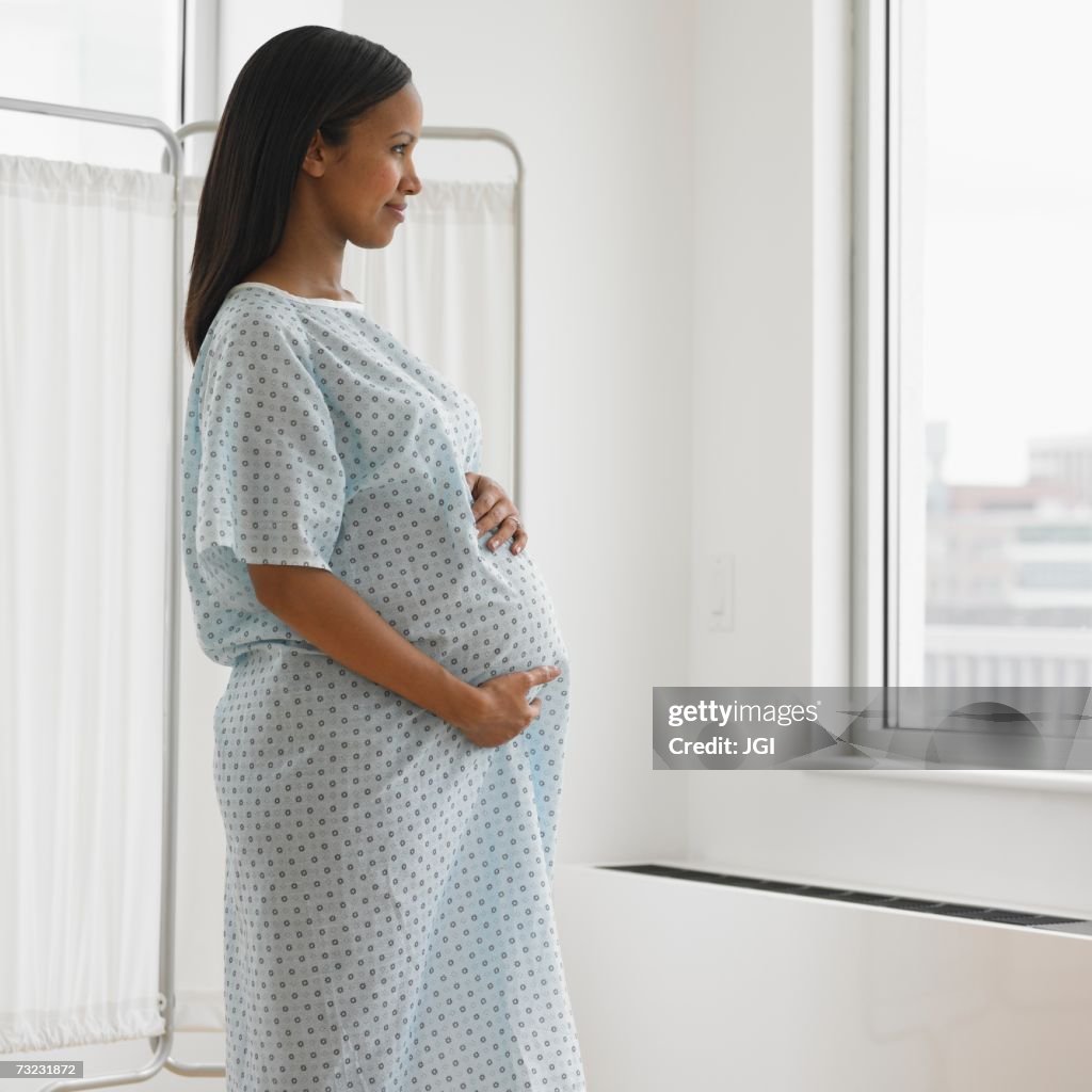 Pregnant African woman in hospital gown looking out window