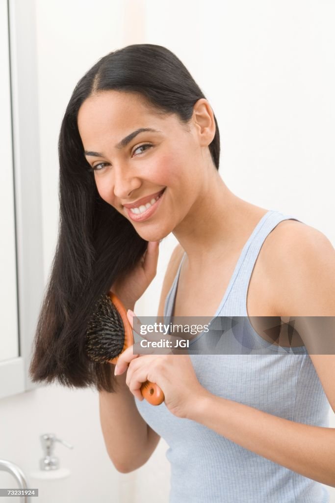 African woman brushing hair in bathroom