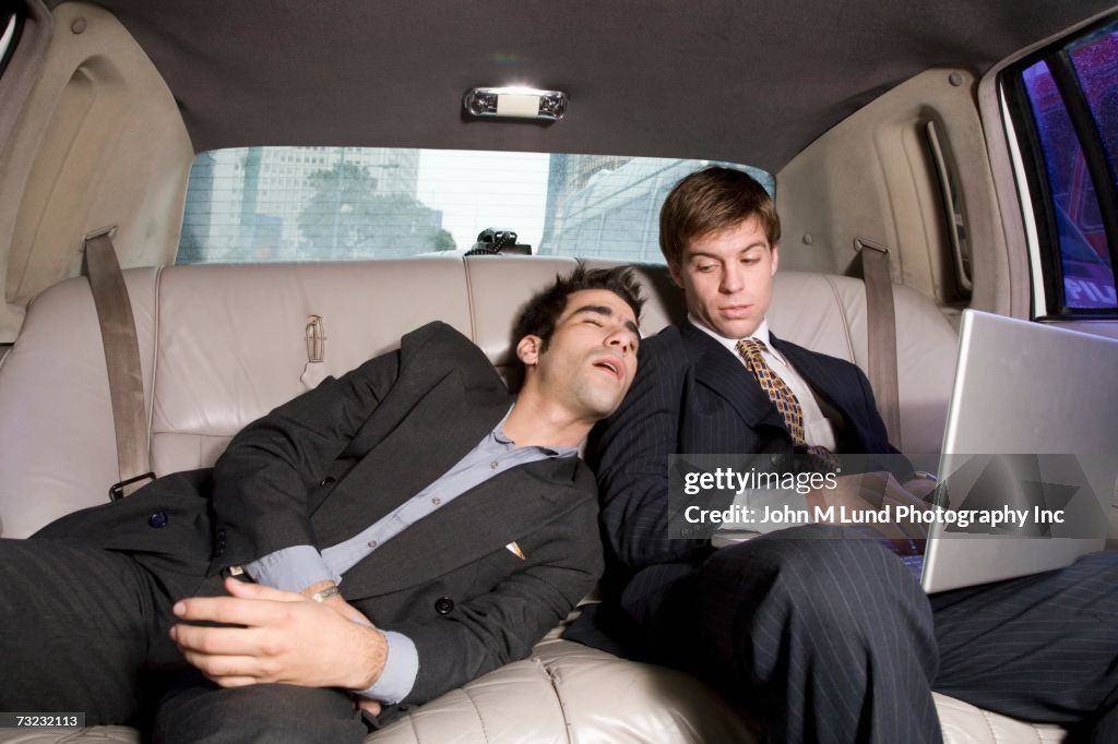 Businessman sleeping on coworker's shoulder in backseat of car