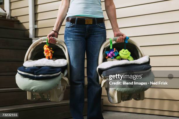 close up of woman holding two baby car seats outdoors - holding two things foto e immagini stock