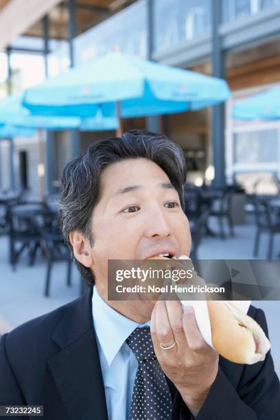 close up of asian businessman eating hot dog outdoors - asian eating hotdog stock pictures, royalty-free photos & images