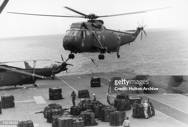 Sea King helicopter hovering above HMS Hermes to airlift ammunition for redistribution to other ships in the convoy, April 1982.
