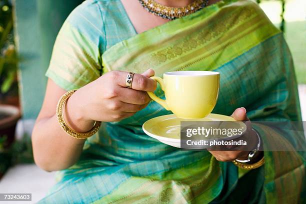 mid section view of a young woman holding a cup of tea - untertasse stock-fotos und bilder