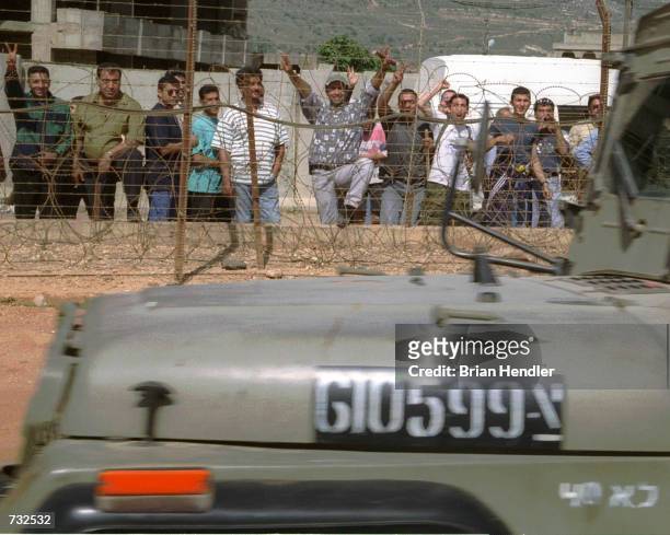 Lebanese citizens cheer with victory signs from behind a fence as an Israeli patrol drives past May 25, 2000 at the Israel-Lebanon border, west of...