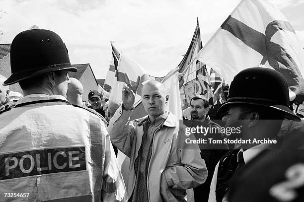 Skinheads from the far-right National Front Party march through Lewisham, south London, under the watchful eye of a black police officer, May 2001.