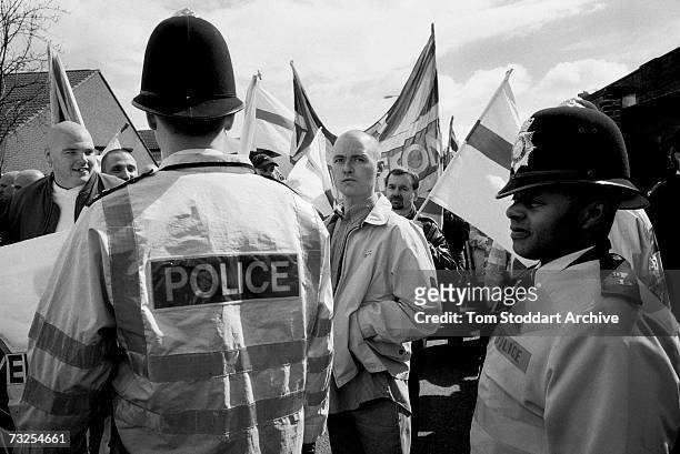 Black police officer looks on as skinheads from the far-right National Front Party march through Lewisham, south London, May 2001.