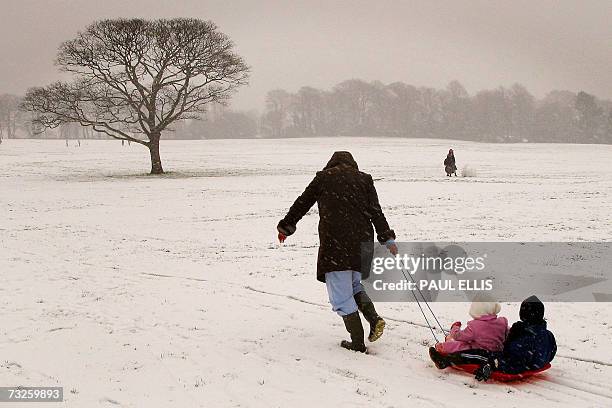Liverpool, UNITED KINGDOM: A woman pulls children on a sled up a snow-covered hill in Liverpool, north-west England, 08 February 2007. Heavy snow...