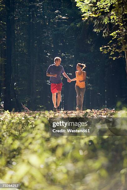 young couple jogging in forest, holding hands - fokus-auf-den-hintergrund stock-fotos und bilder