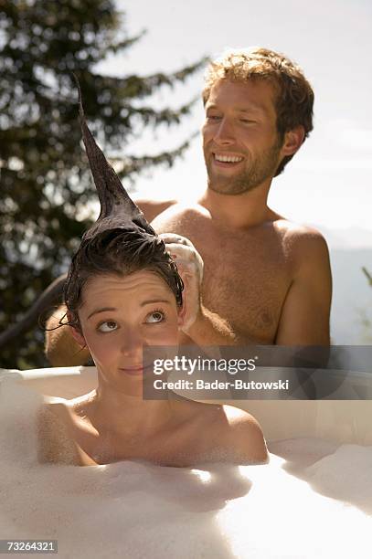 young woman lying in bathtub, young man washing hair - couples showering stock-fotos und bilder