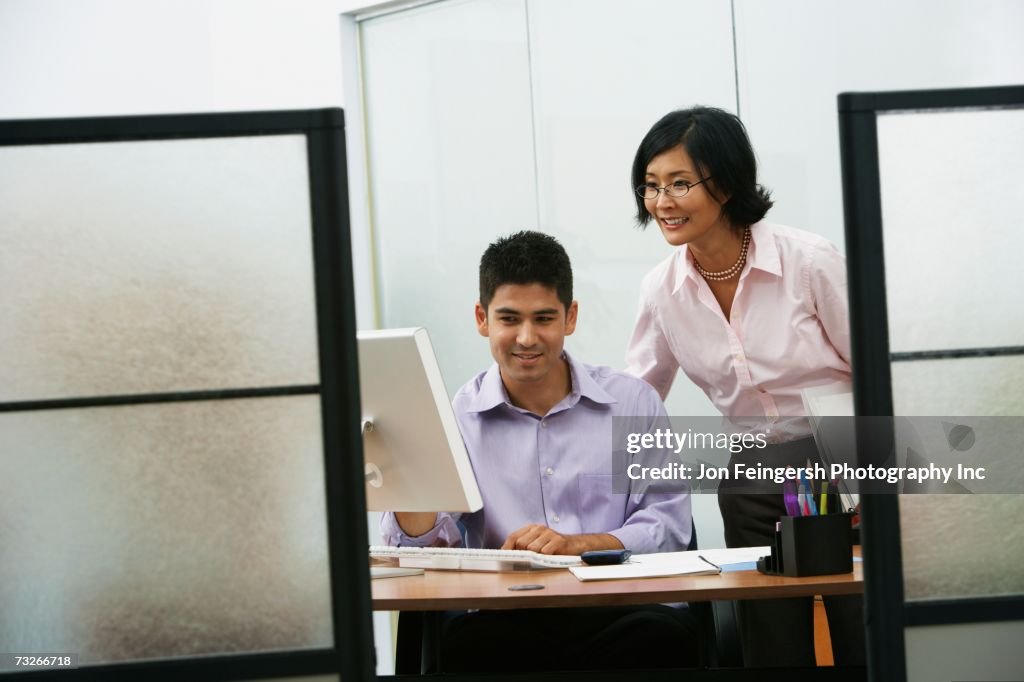 Asian businesswoman and businessman looking at computer in office