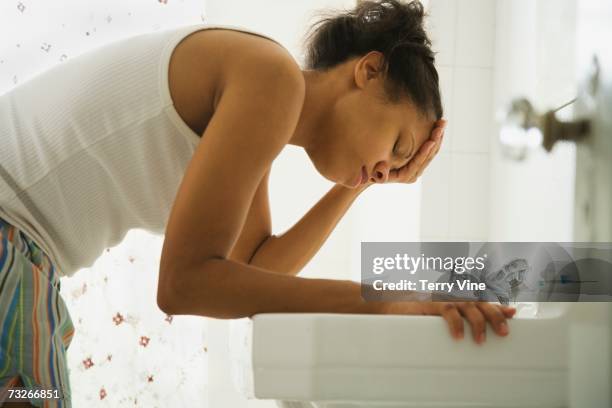 african woman leaning over bathroom sink with head in hand - headache imagens e fotografias de stock